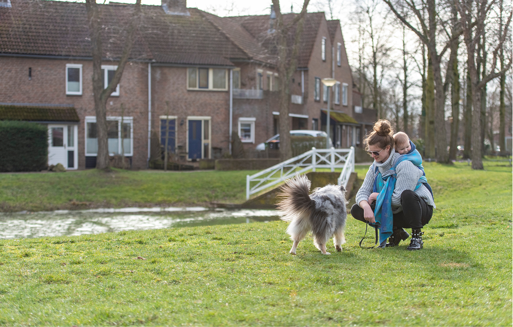 Vrouw met kind en hond op een grasveld voor woningen