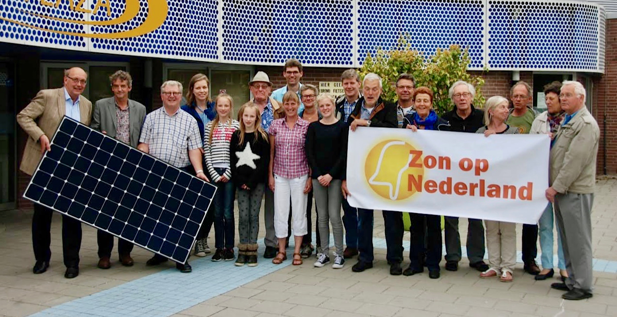 Groep coöperatieleden met zonnepaneel en spandoek Zon op Nederland